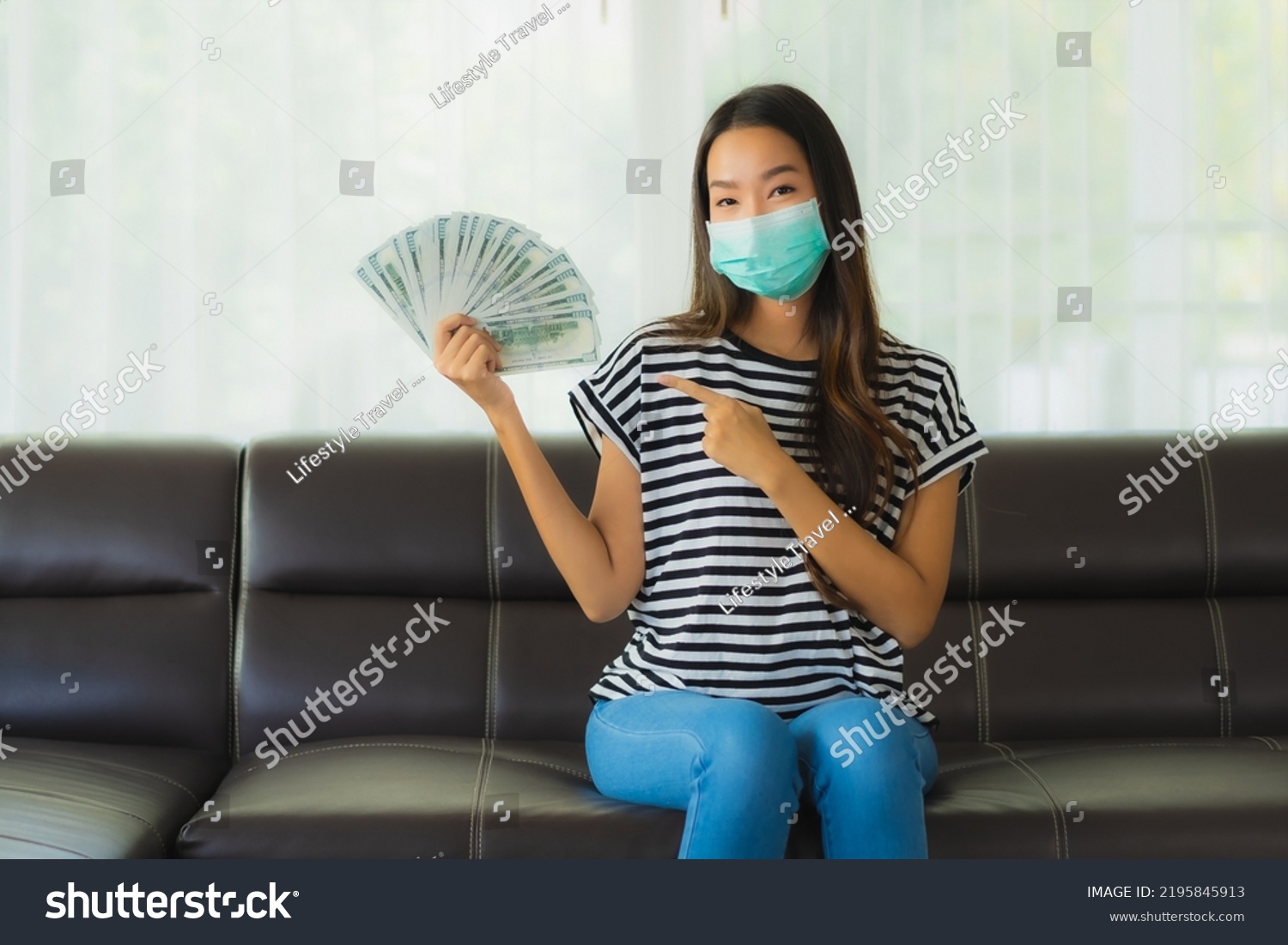 Portrait beautiful young asian woman with mask on sofa show money or cash at home #2195845913