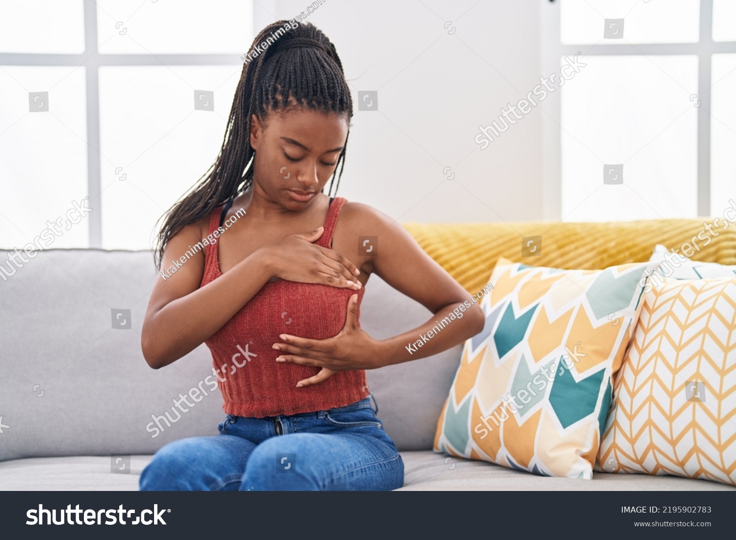 African american woman examining breast with hand sitting on sofa at home #2195902783