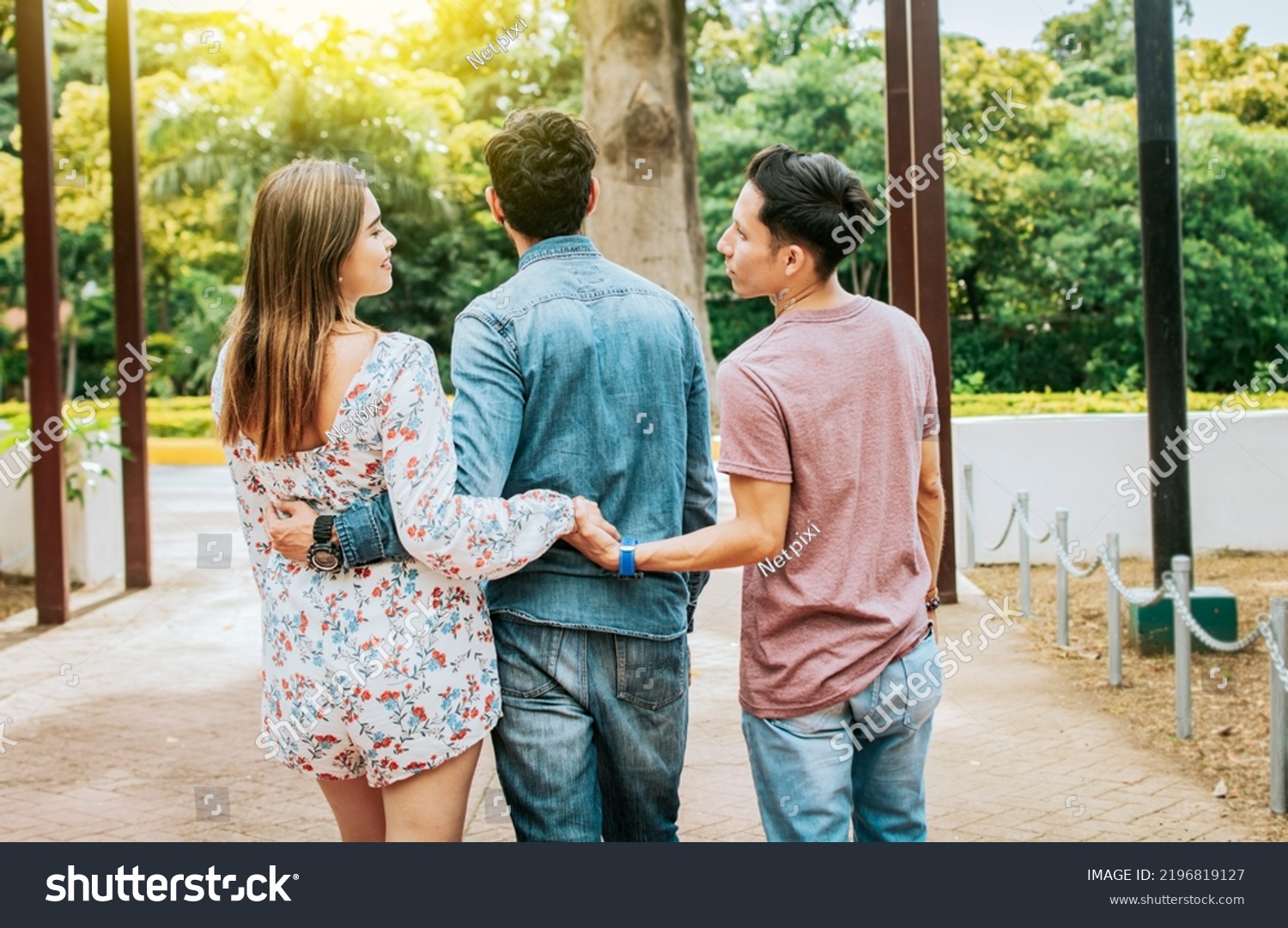 Unfaithful girl walking in the park with her boyfriend while holding another man hand. Love triangle concept. Woman holding hands with another man while walking with her boyfriend outdoor #2196819127