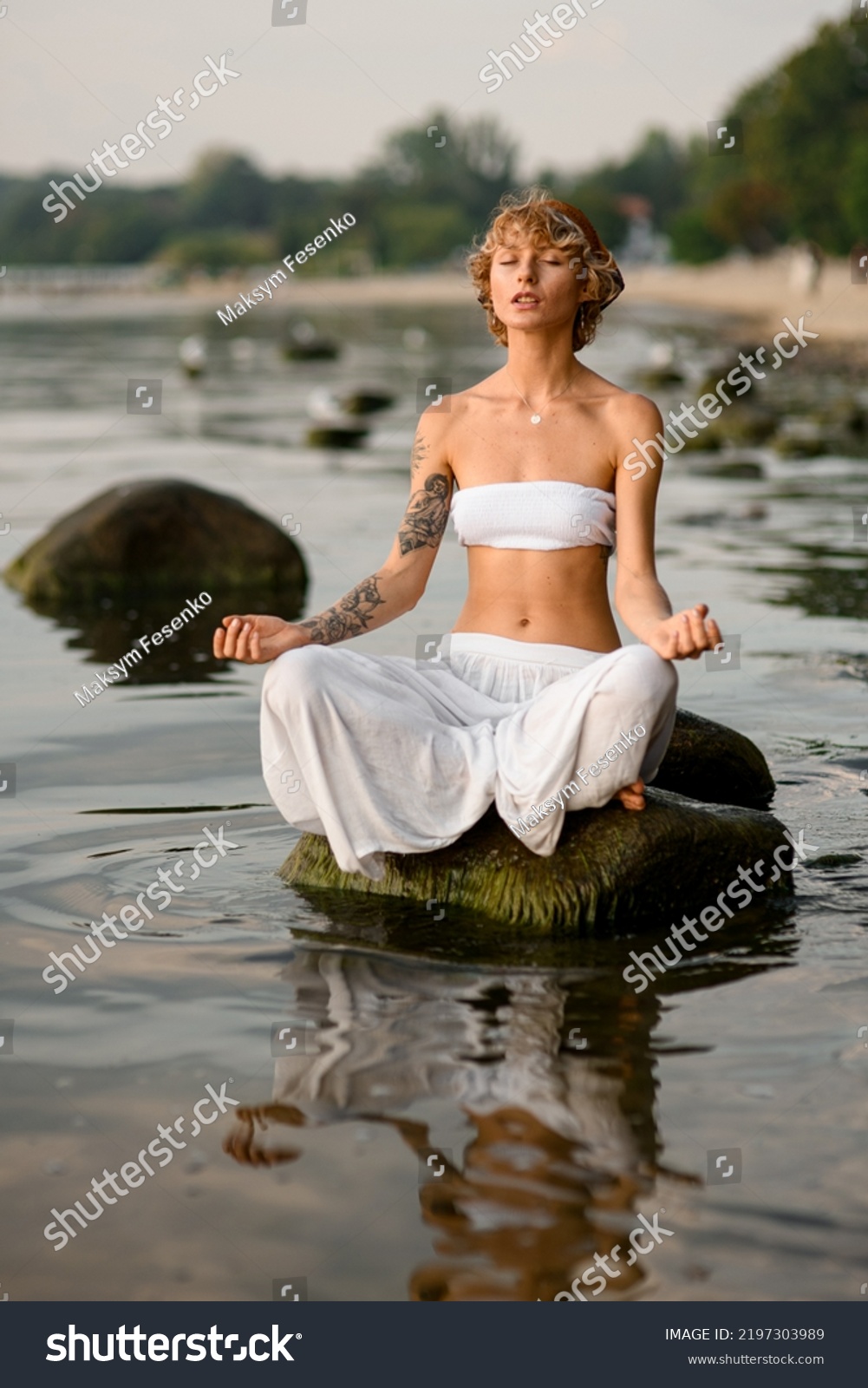 peaceful woman practices yoga position doing meditation in tranquil outdoor sitting on stone in water. Mental wellbeing healthy lifestyle. #2197303989