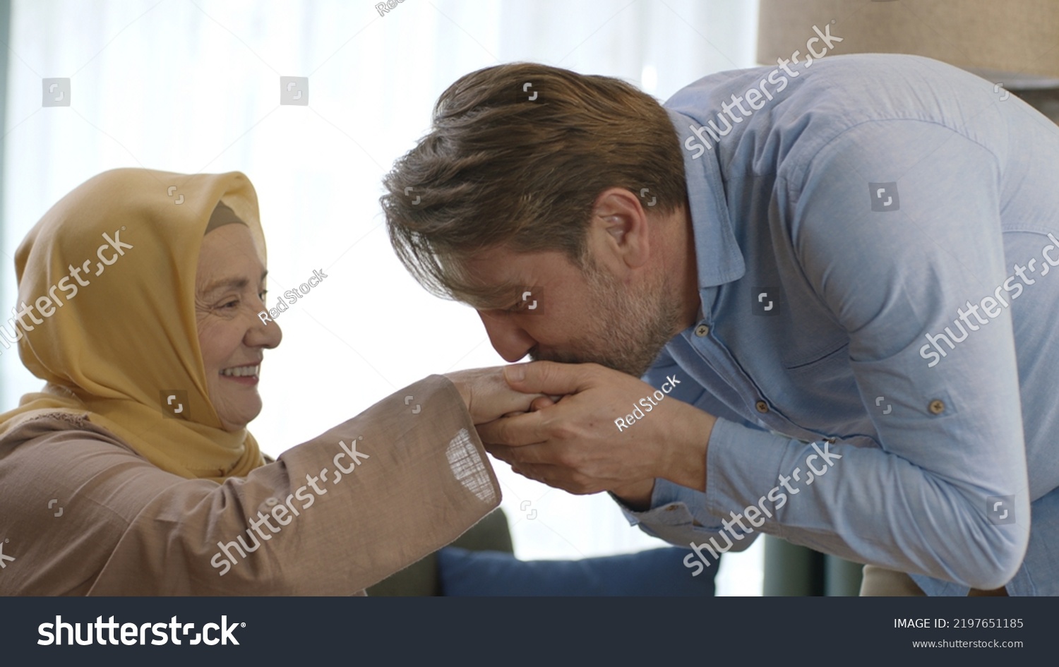 Young man kisses his mother's hand during Eid Mubarak (Turkish Ramadan or Şeker Bayram).The man kisses her hand to show respect to her veiled mother.Muslim holiday traditions concept. #2197651185