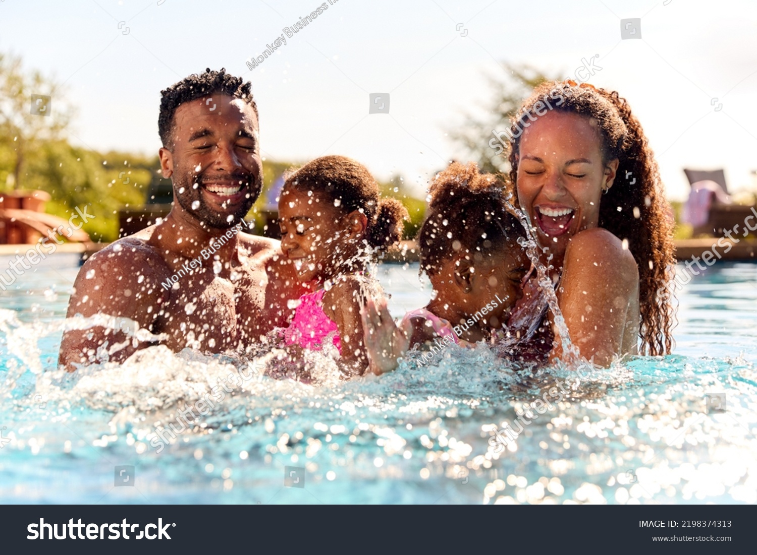 Family On Summer Holiday With Two Girls Being Held In Swimming Pool By Parents And Splashing #2198374313