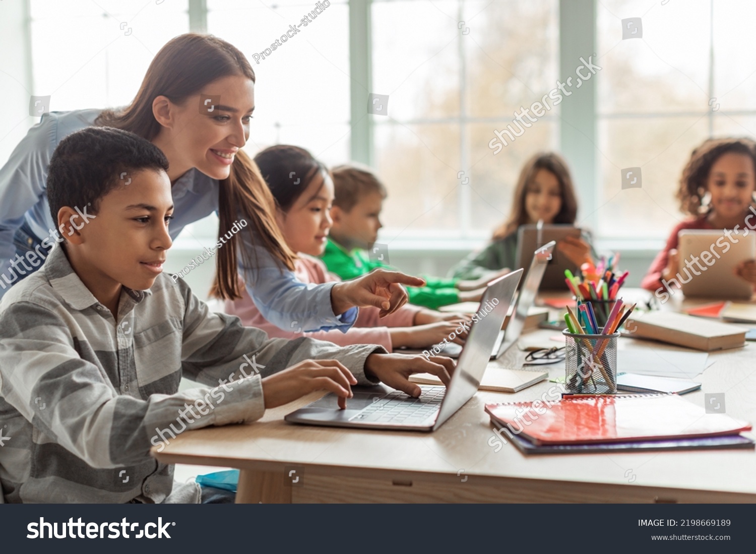 Teacher Teaching Diverse School Kids Using Laptop In Classroom. African American Schoolboy And Diverse Classmates Browsing Internet On Computer Learning Online Indoor. E-Learning Concept #2198669189