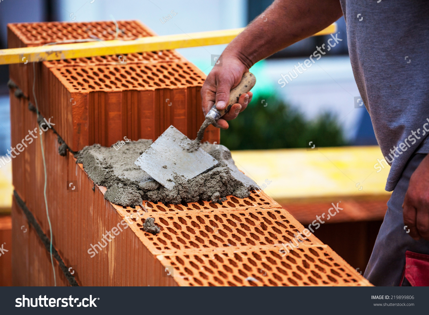 anonymous construction worker on a building site when building a house built a wall of brick. brick wall of a solid house. symbolic image for illegal work and bungling #219899806