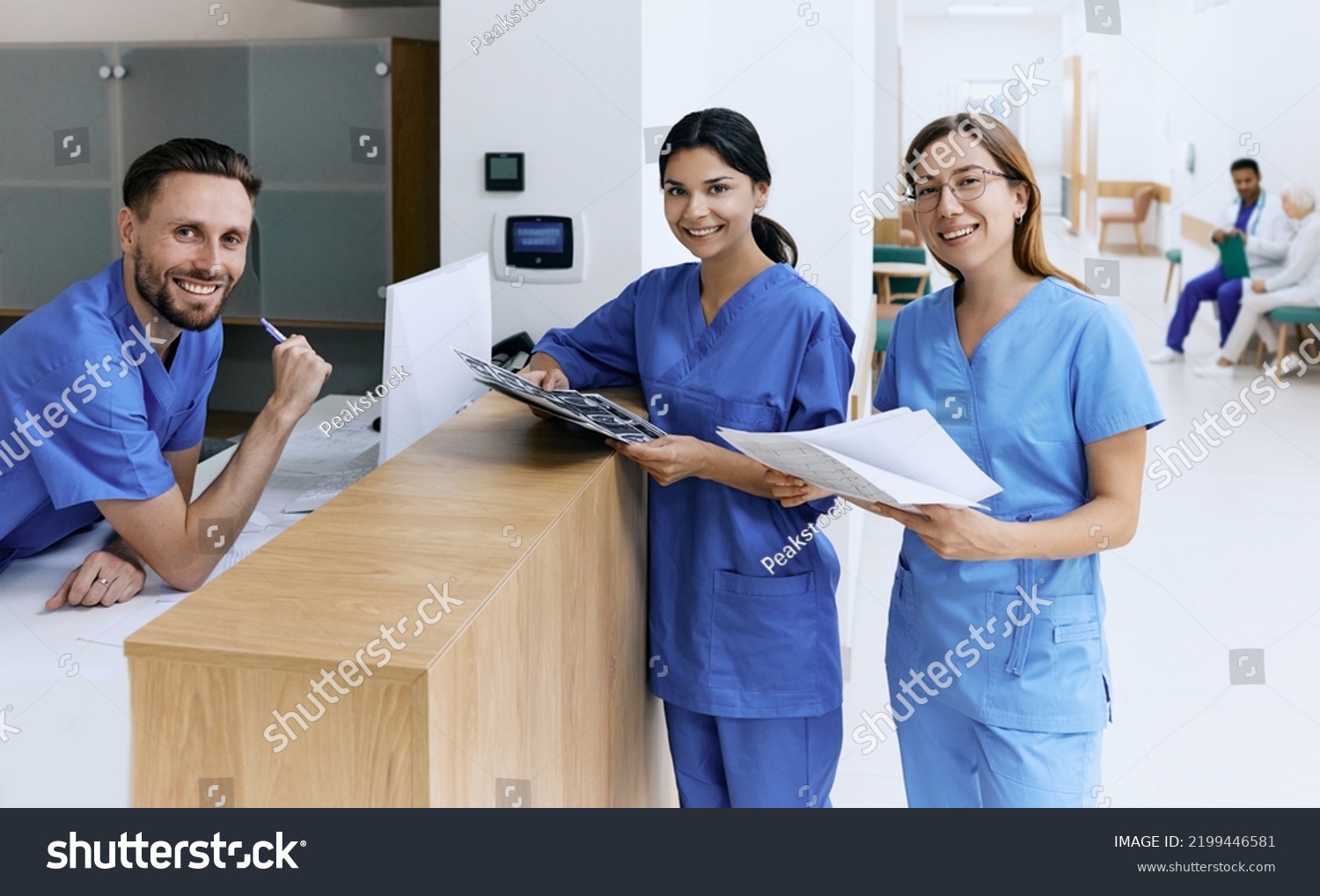 Nurse on duty talking with medical assistants during working day in medical clinic standing near reception desk at hospital lobby. Medical staff of clinic #2199446581