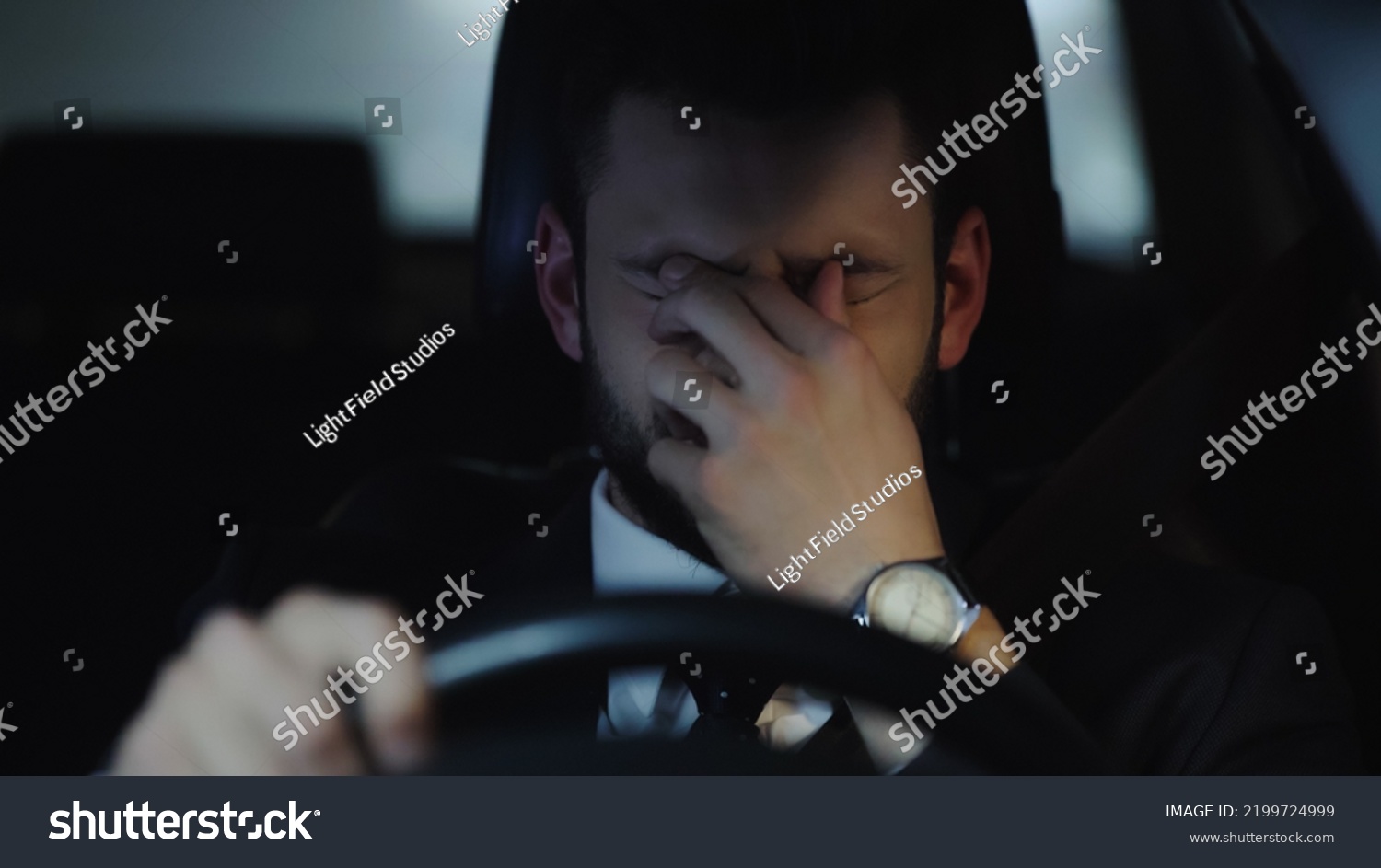 sleepy businessman touching eyes while driving car in evening #2199724999