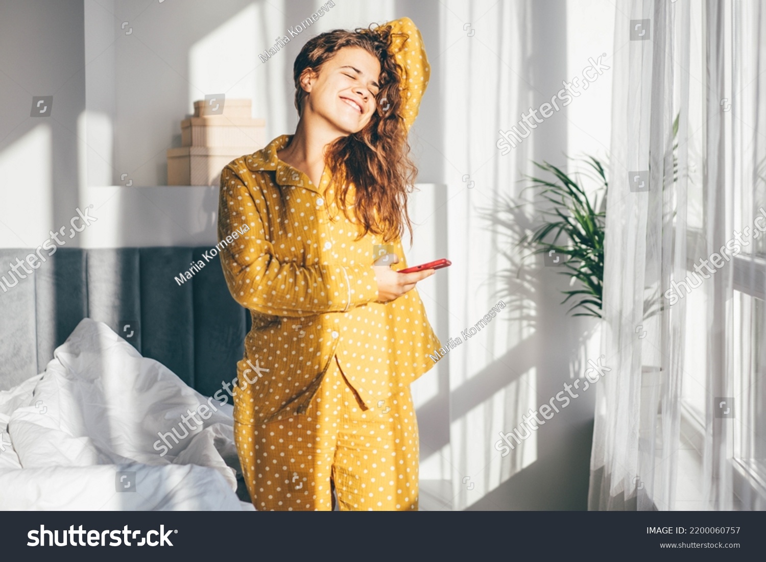 Woman in yellow pajamas hugging pillow and smiling.  #2200060757