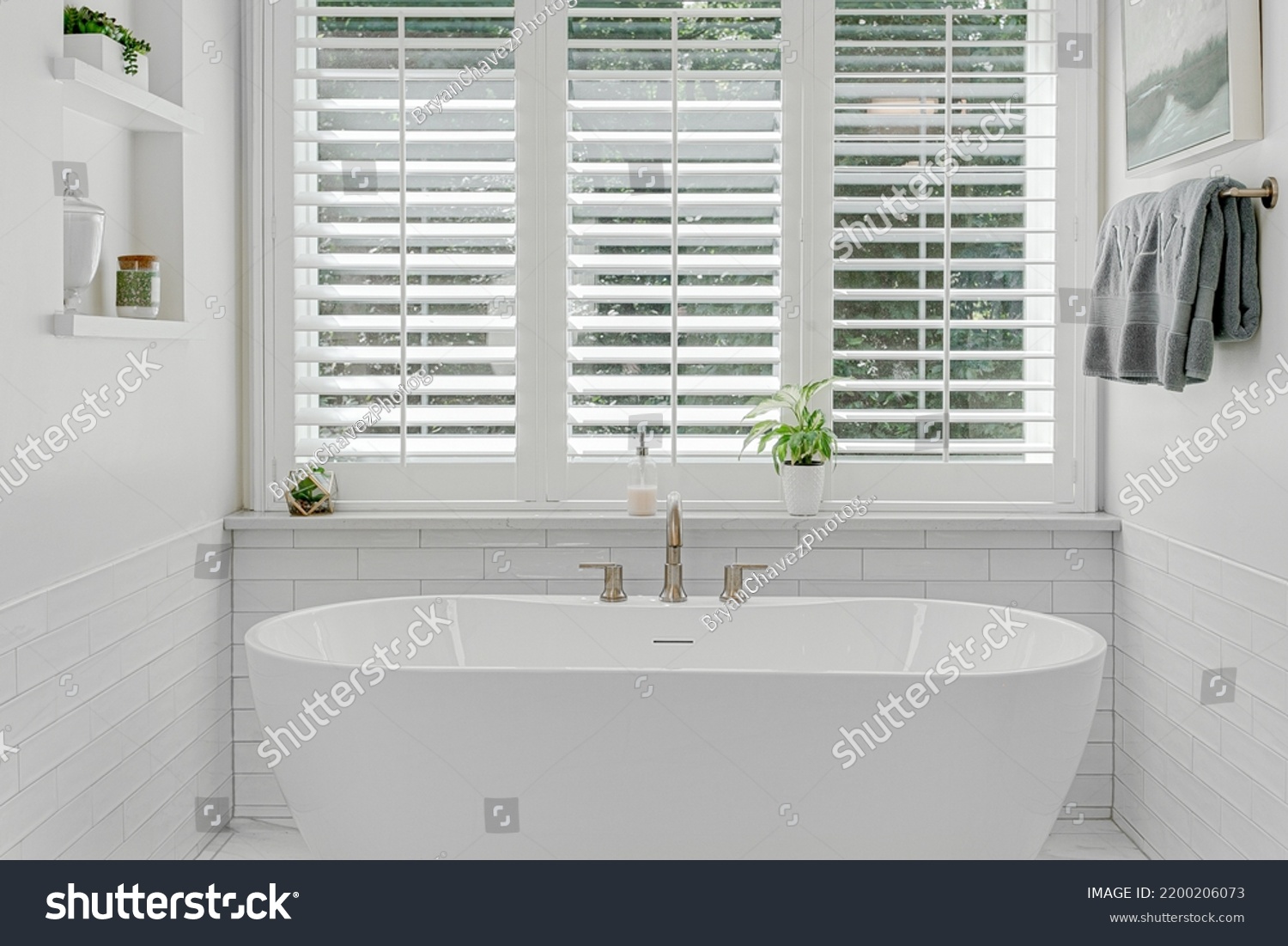 Modern luxury soaking tub with brass faucet interior design staged with plantation shutters #2200206073