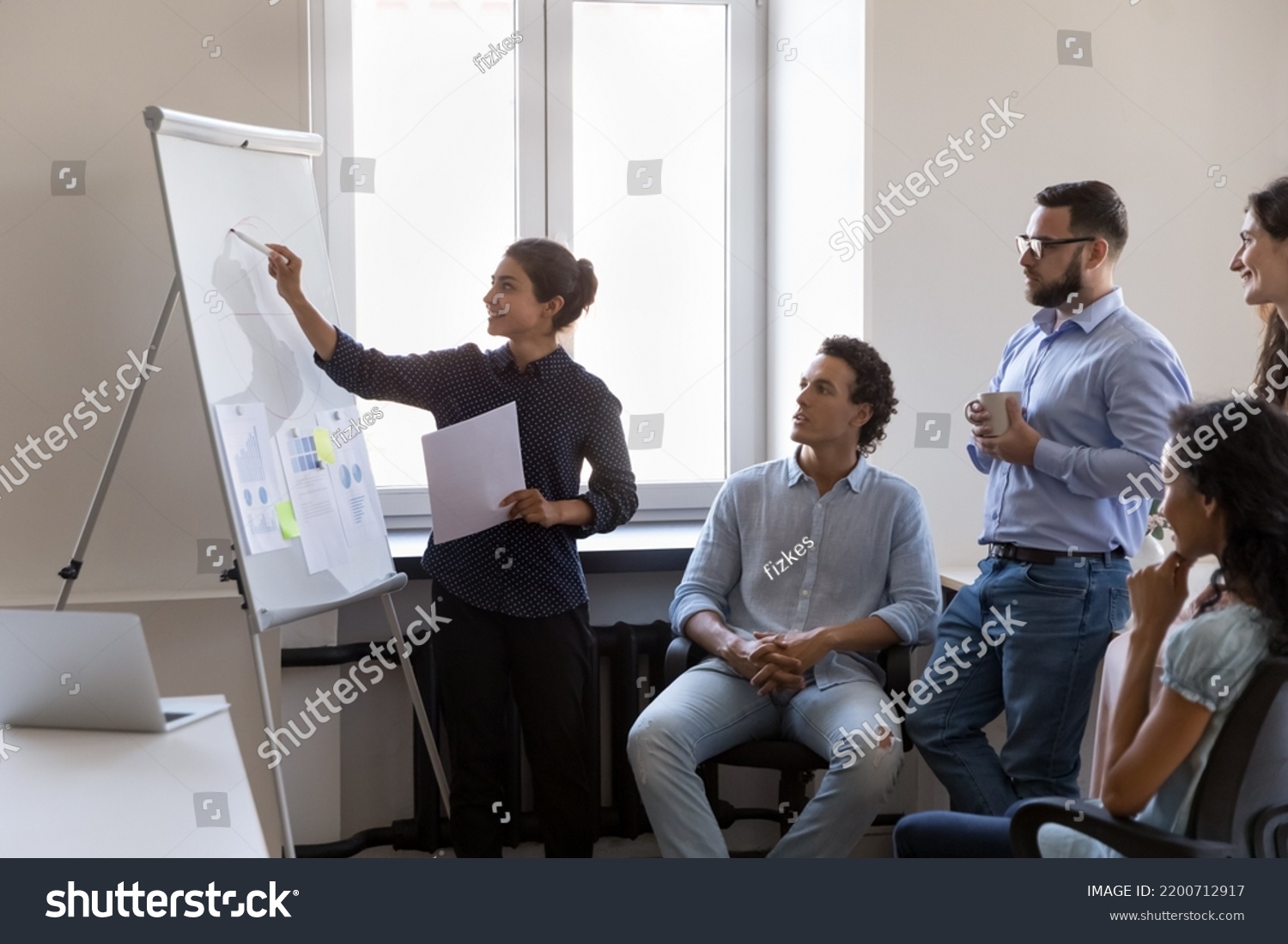Indian business teacher woman training diverse group of interns, drawing marketing chart on whiteboard, explaining data, teaching students. Multiethnic team leader presenting report #2200712917