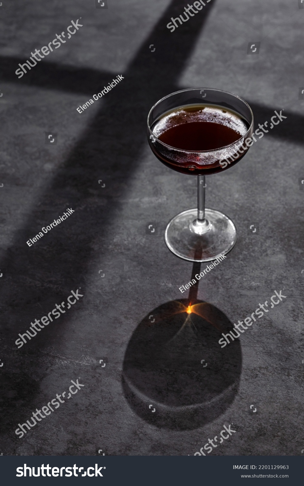 A coupe cocktail glass of red vermouth or liqueur shot with hard back light on grey background #2201129963