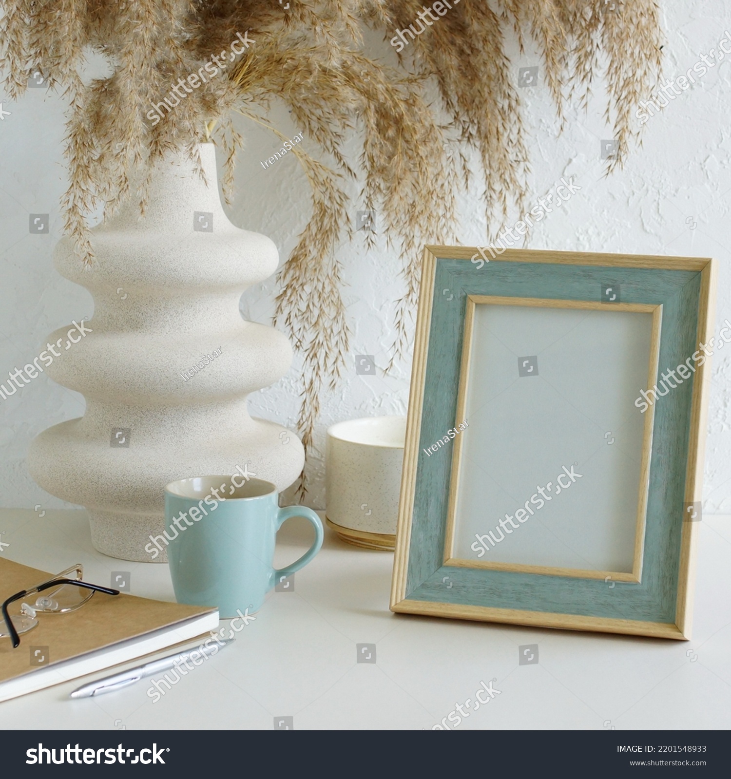 Modern home office workspace with photo frame mockup.  Aesthetic scandy hygge style.Cup coffee, photo frame,planner, vase with grass,aroma candle .Copy space.Neutral colors home design. #2201548933