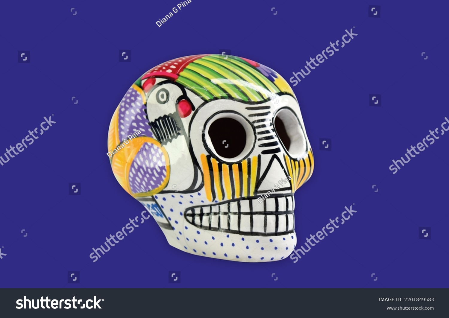 Beautiful and colorful Mexican skull isolated, made of ceramic, and painted by hand. Craft made in Mexico. Purple background. Traditional mexican skull for the Day of the Deads. #2201849583