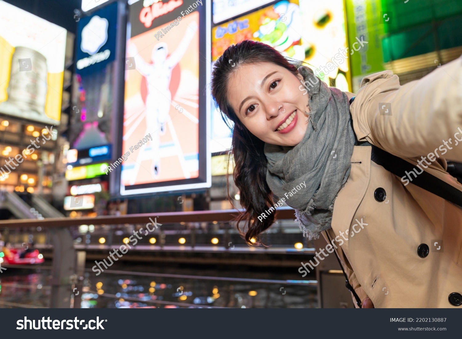 cheerful Asian Japanese girl taking self portrait picture with the illuminated glico man at background near doutonbori river and Shinsaibashisuji shopping street in Osaka japan at night #2202130887