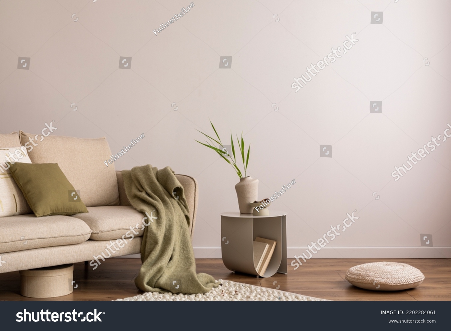 Interior design of living room with copy space, beige sofa, side table, leaf in vase, pouf, elegant accessories and boucle rug. Beige wall. Minimalist home decor. Template.  #2202284061