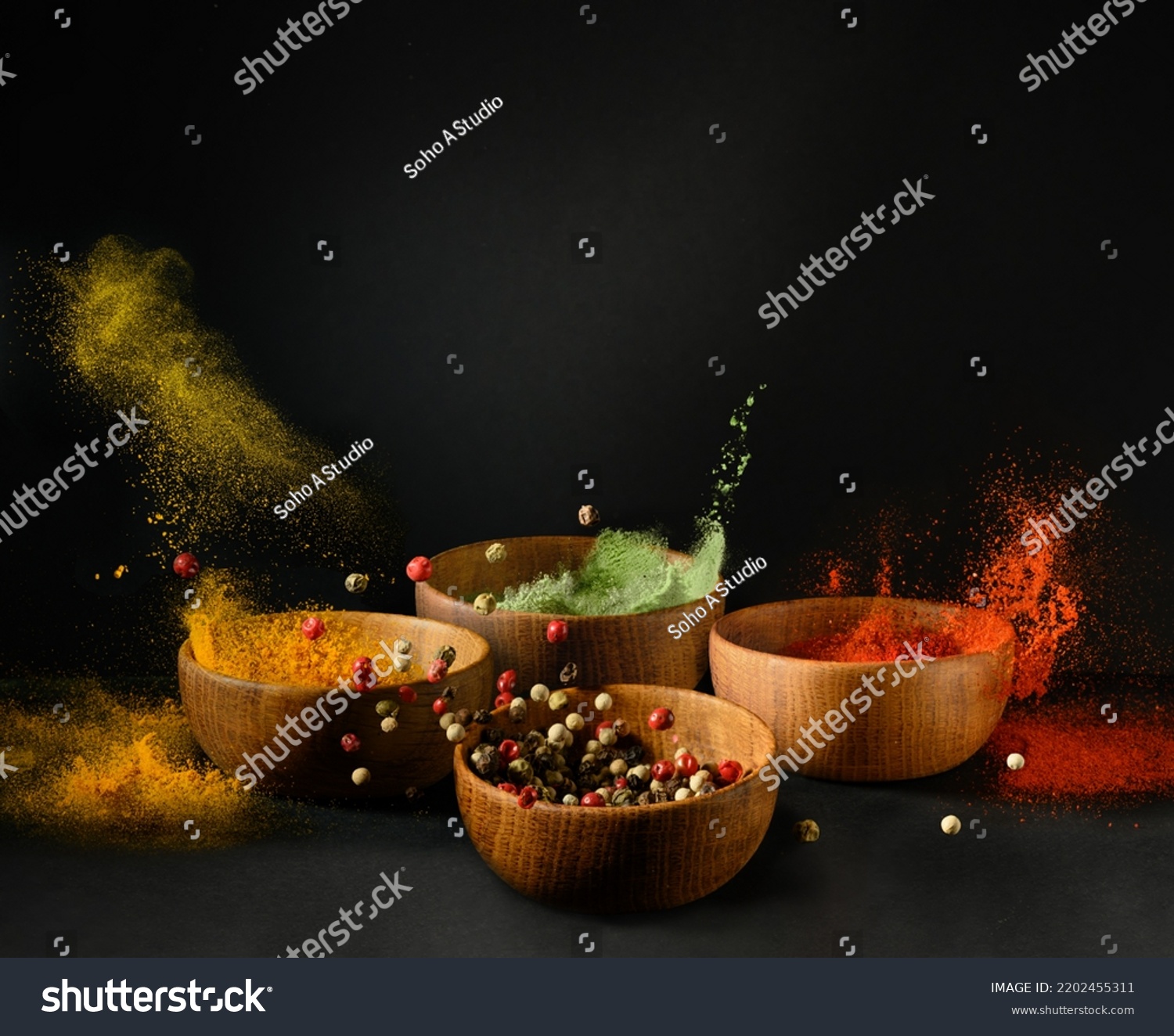 Spices and seasonings powder splash, explosion. Set of colorful spices in wooden bowls, isolated on black background. Freeze motion photo #2202455311