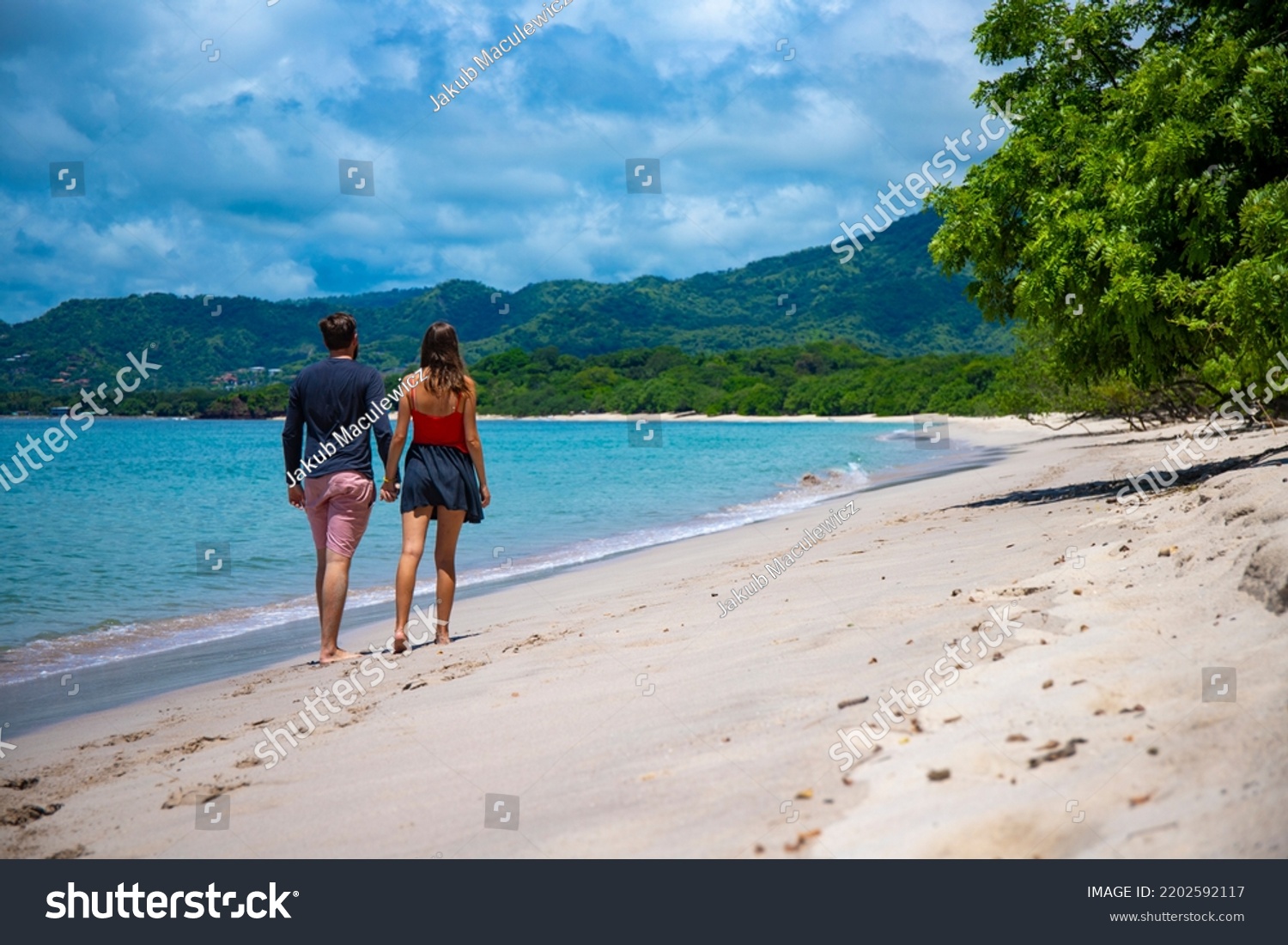 young couple walks holding hands on the beautiful beach in costa rica #2202592117