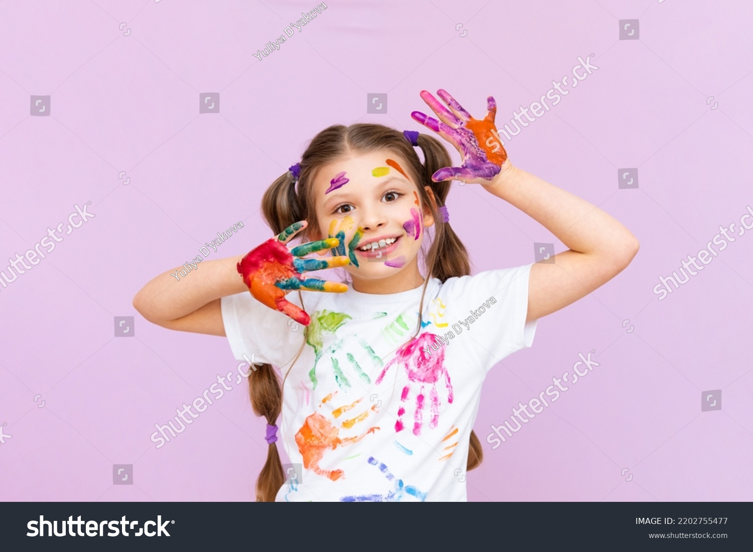 A little girl painted with multicolored paints will playfully have to create on a pink isolated background. Development of children's creativity for schoolchildren. #2202755477