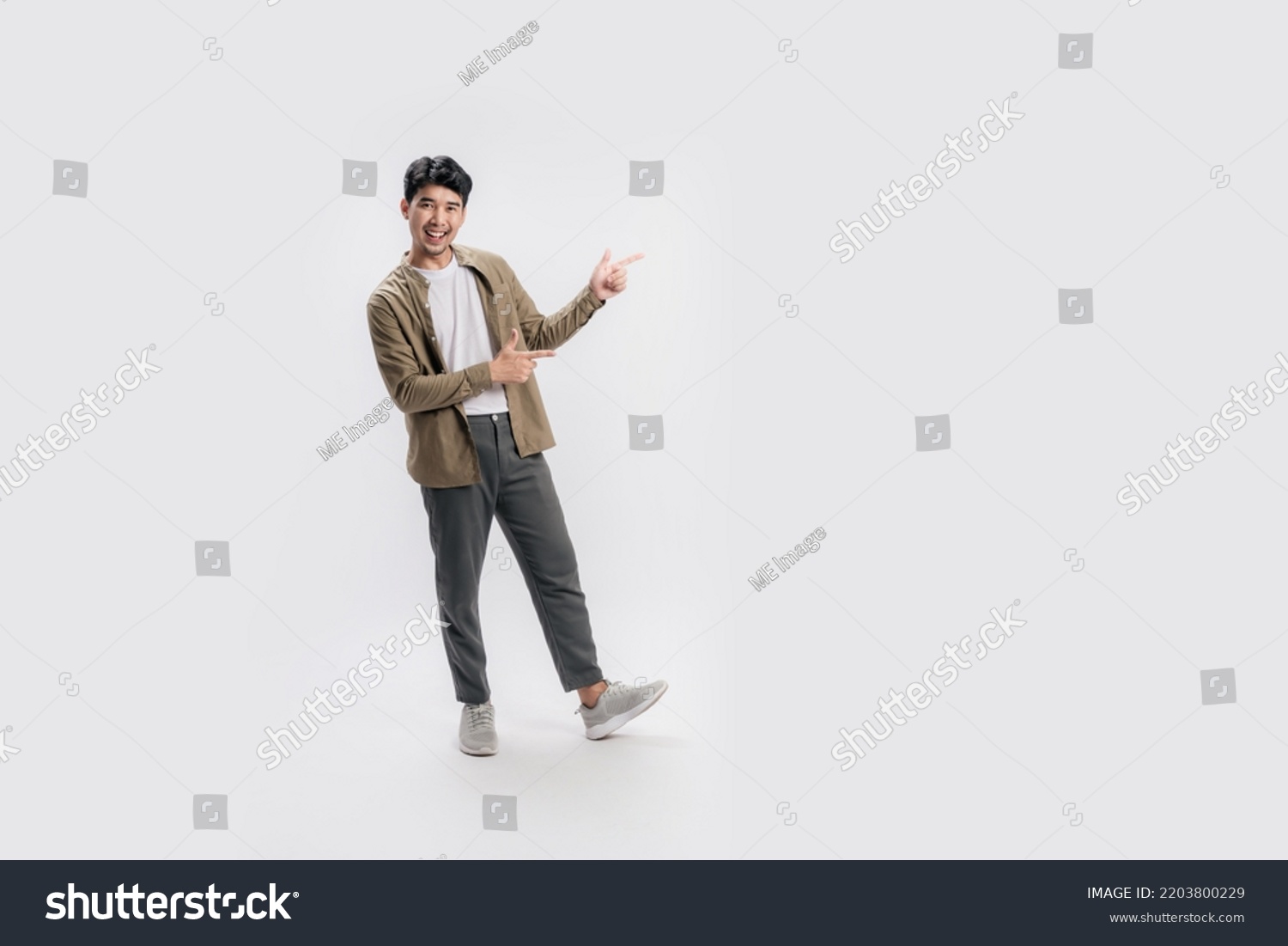 Full length of a handsome asian man pointing out to present something, the smile on his face, his hand gesture and the casual outfit are perfect for the suggestion to copy space. #2203800229