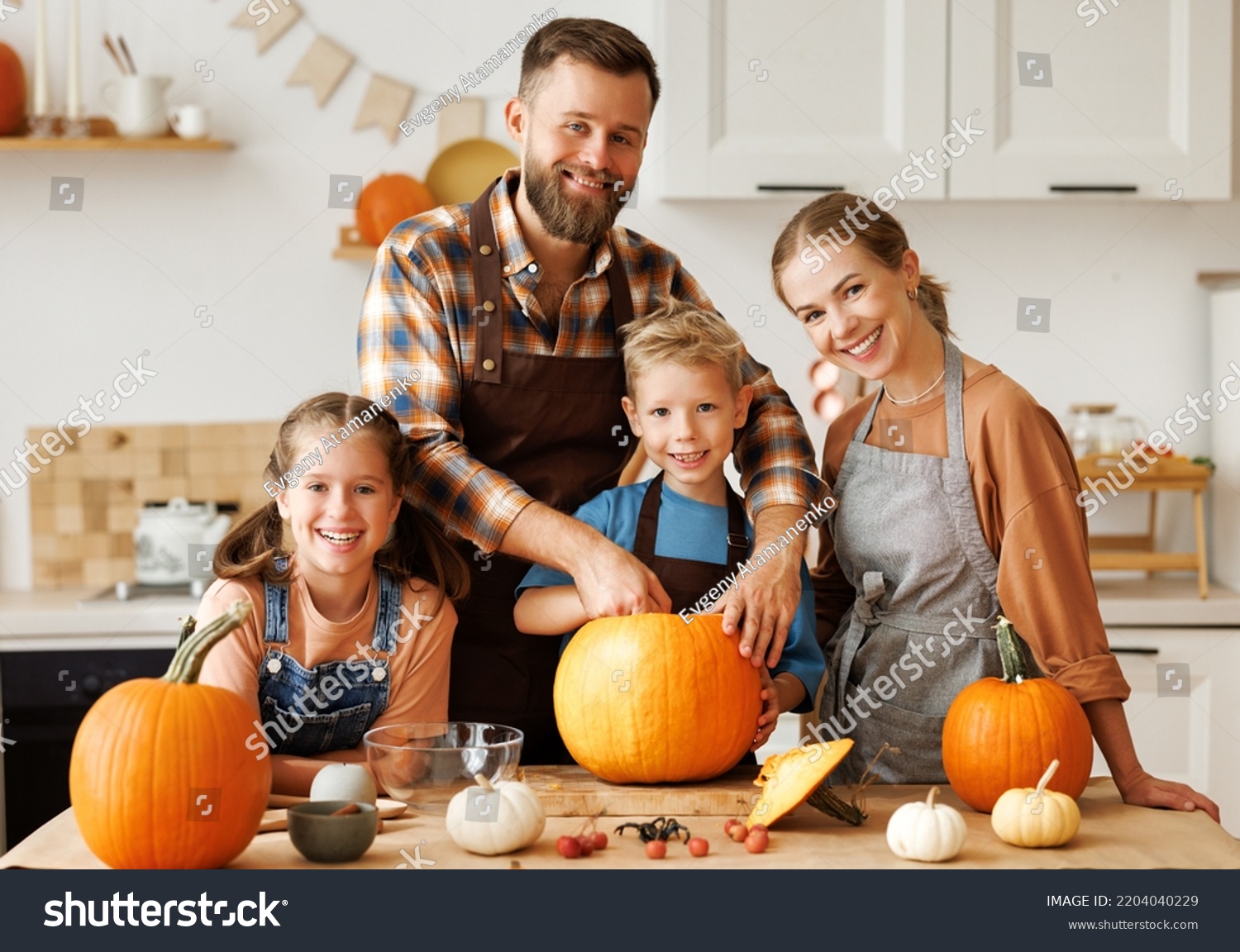 Happy family mother, father  and children daughter and son to remove   pulp from pumpkin while carving jack o lantern with family in cozy kitchen at home, parents with kids preparing for Halloween #2204040229