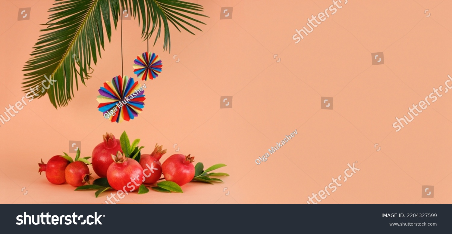 Pomegranates, palm leaves with colorful holiday decorations on a coral background, Rosh Hashanah and Sukkot concept. Banner with space for text #2204327599