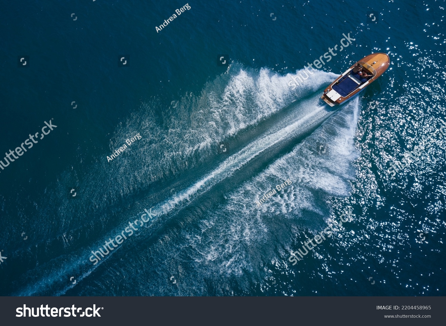 Luxurious wooden boat fast movement on dark water. Luxurious wooden motor boat rushes through the waves of the blue Sea. Classic Italian wooden boat fast moving aerial view. #2204458965