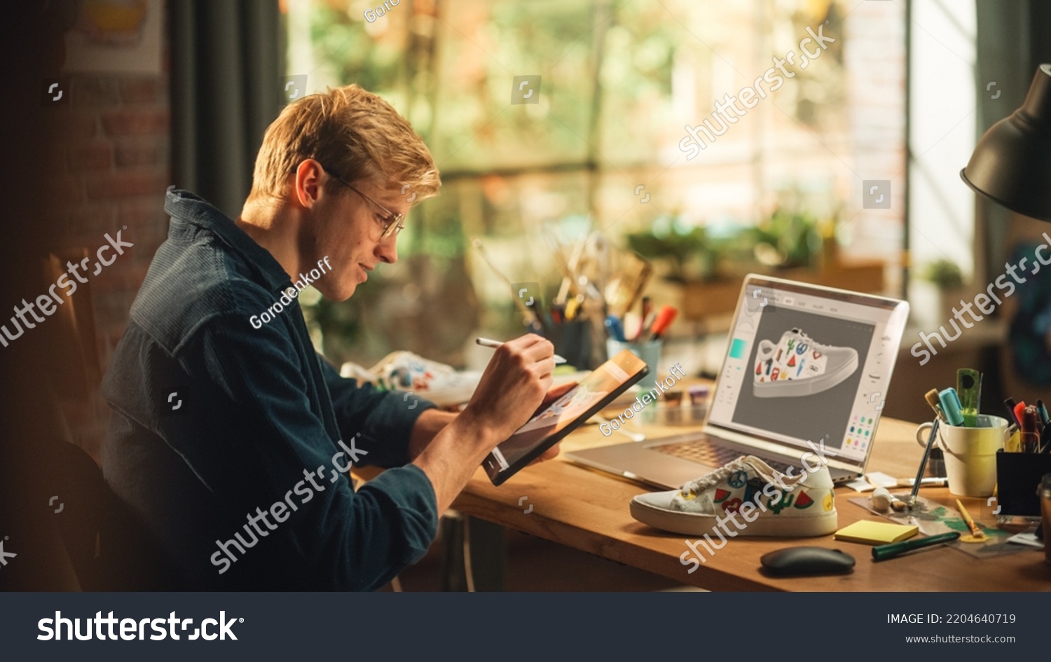 Experienced Male Teen Designer Works With Digital Graphics Tablet Touchscreen, Drawing Sketch of a New Unique Shoes Design. 3D Prototype of his Product in Editing Software on Laptop Display. #2204640719