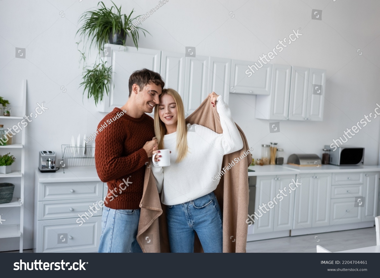 caring man holding blanket near pleased girlfriend in sweater with cup of tea #2204704461