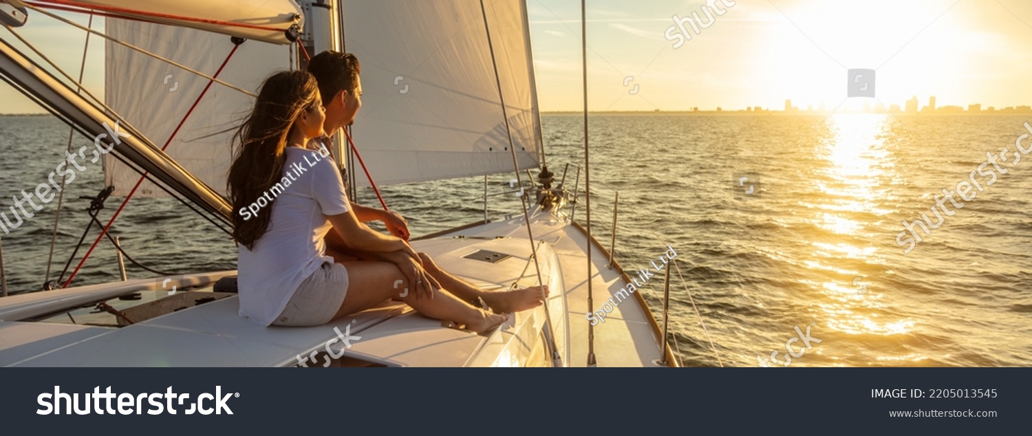 Panorama of young Hispanic couple at leisure sailing the ocean relaxing on luxury yacht watching the sunset on the horizon #2205013545