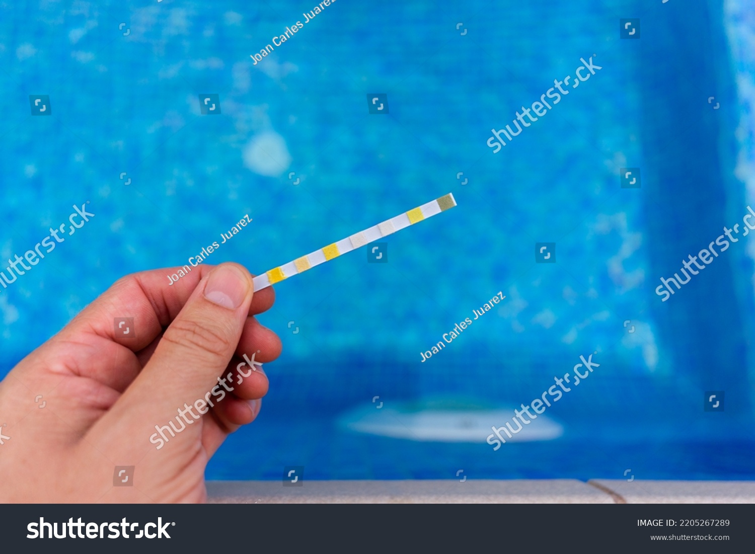 Hand with measuring pool strips to check water quality in a swimming pool #2205267289