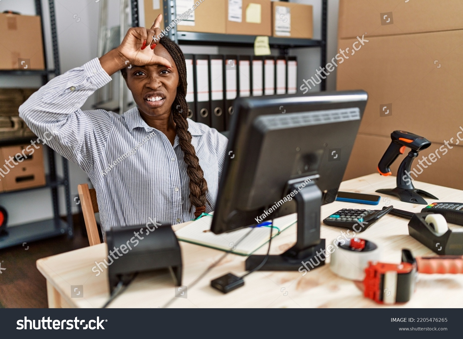 African woman working at small business ecommerce making fun of people with fingers on forehead doing loser gesture mocking and insulting.  #2205476265