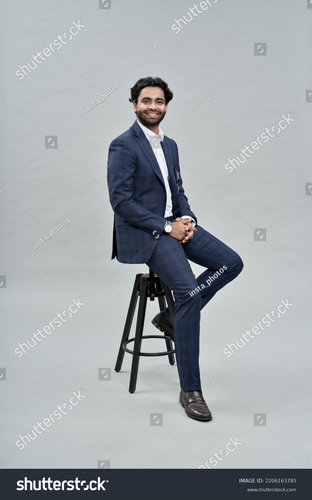 Happy successful rich young indian business man ceo leader, wealthy arab professional manager, confident male businessman executive wearing suit sitting on chair isolated on beige, vertical portrait. #2206163785