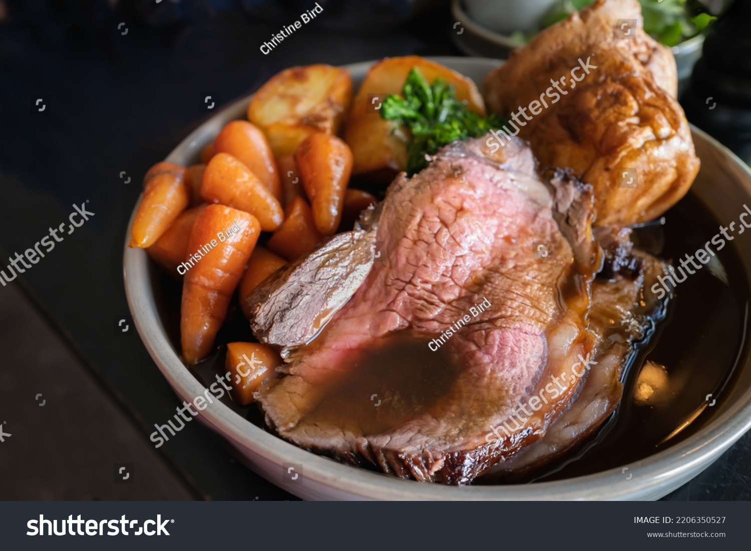 Roast beef slices on a plate with carrots, roast potatoes, a Yorkshire pudding and gravy, making a complete Sunday roast meal.  #2206350527