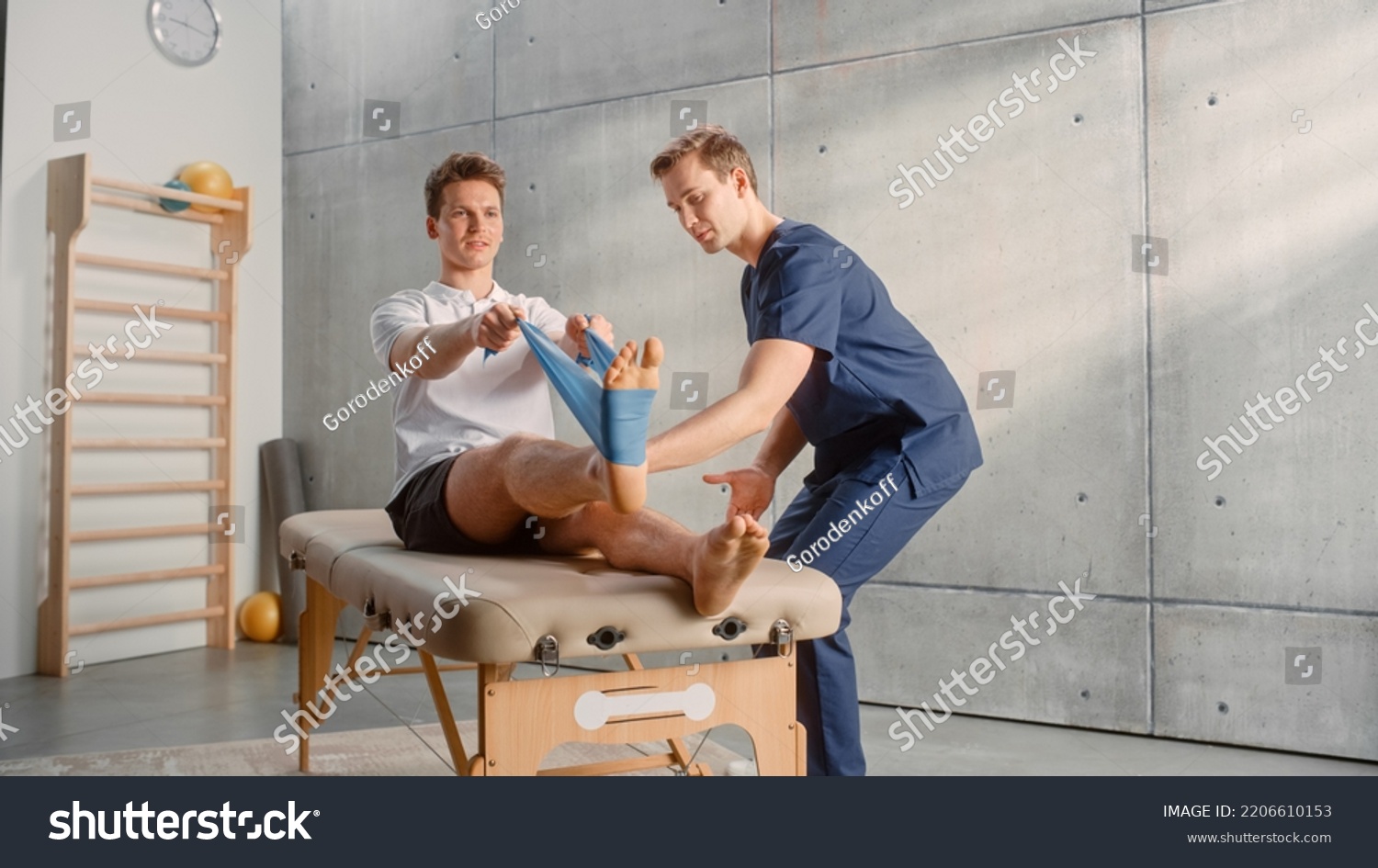 Young Male Athlete Undergoing Physiotherapy, Professional Sport Masseur Helping with Foot Exercise with a Rubber Band. Musculoskeletal Pain Therapy and Rehabilitation in Modern Clinic Concept. #2206610153