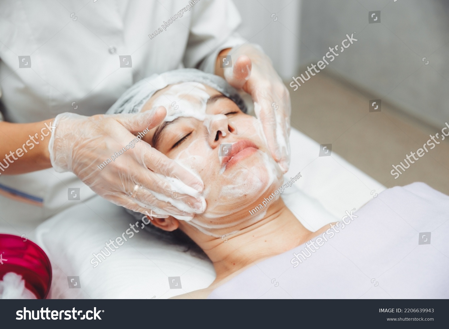 the cosmetologist cleanses the skin with foam. A woman's skin care procedure. Natural cosmetics. A beautiful face. Cosmetic treatment of the face. Therapeutic peeling cream. #2206639943