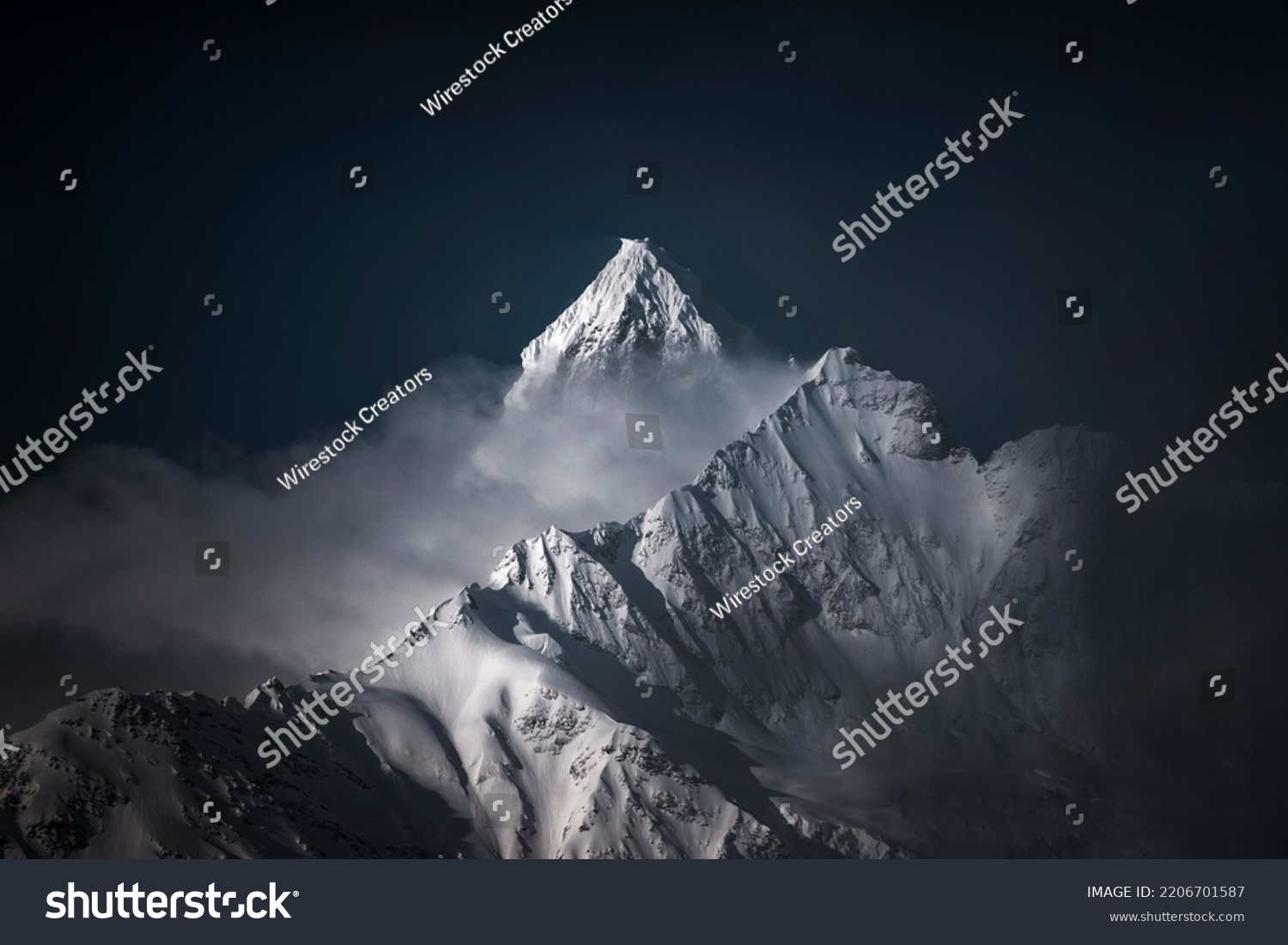 A high-angle shot of snowy mountains covered with clouds during a dark evening #2206701587