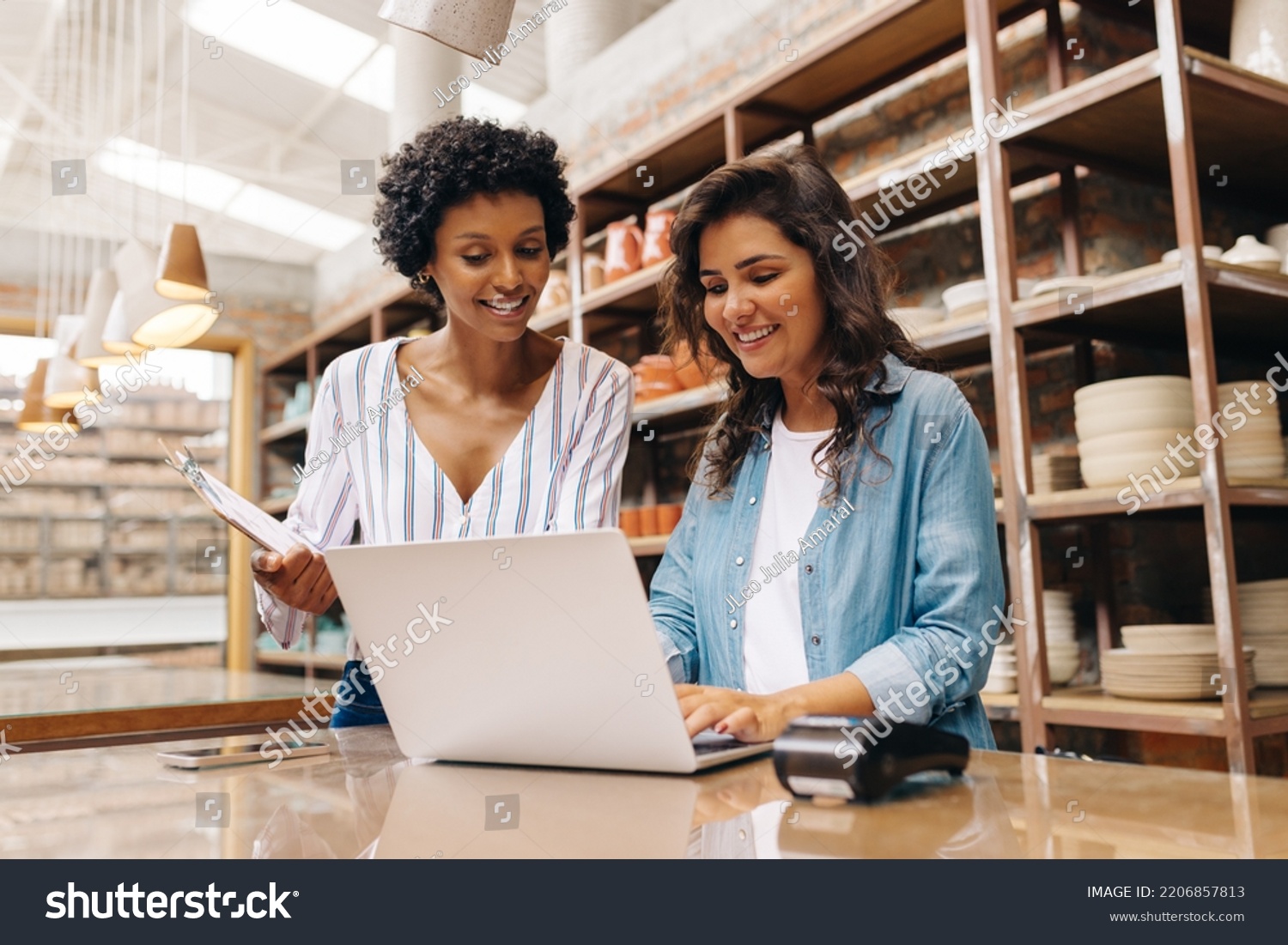 Happy young ceramists using a laptop while working in their store. Female entrepreneurs managing online orders on their website.Cheerful young businesswomen running a creative small business together. #2206857813