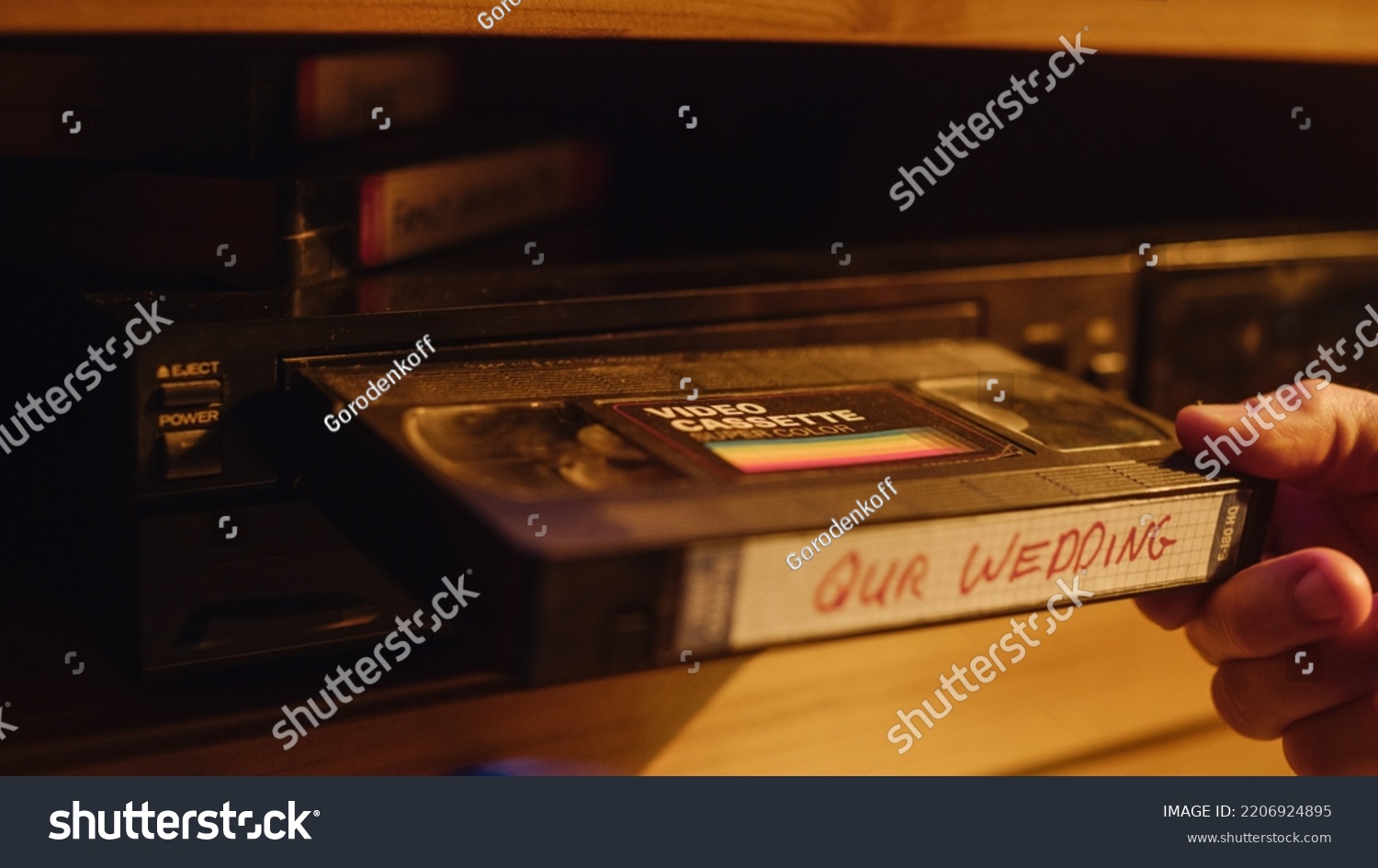 Close Up of a Person Inserting a VHS Cassette in a Player with Nostalgic Wedding Footage from Home Video Camera. Retro Nineties Technology Concept. Old VCR with Shallow Depth of Field and Bokeh. #2206924895