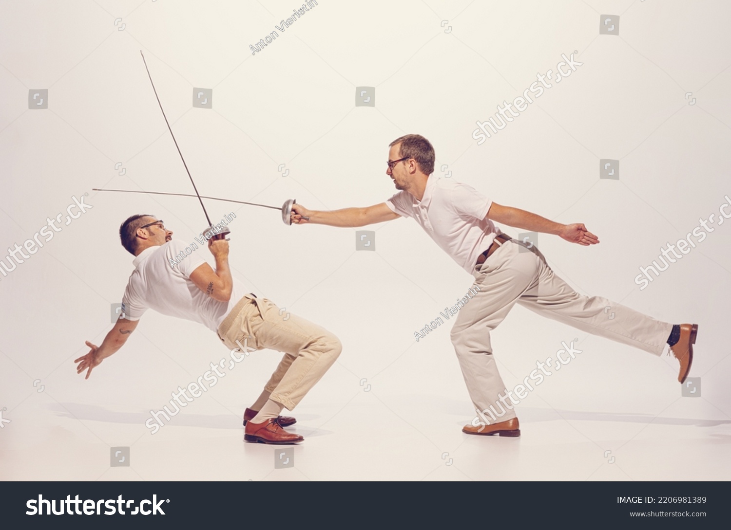 Portrait of two men in a suit fighting with swords isolated over grey studio background. Dynamic image. Concept of sport, hobby, emotions, active lifestyle, retro fashion. Copy space for ad #2206981389