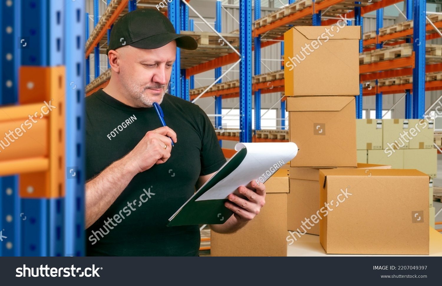 Storekeeper making revision. Man storekeeper in front of cardboard boxes. Warehouse worker thought. Guy with pen next to warehouse racks. Storekeeper man takes care of incoming goods #2207049397