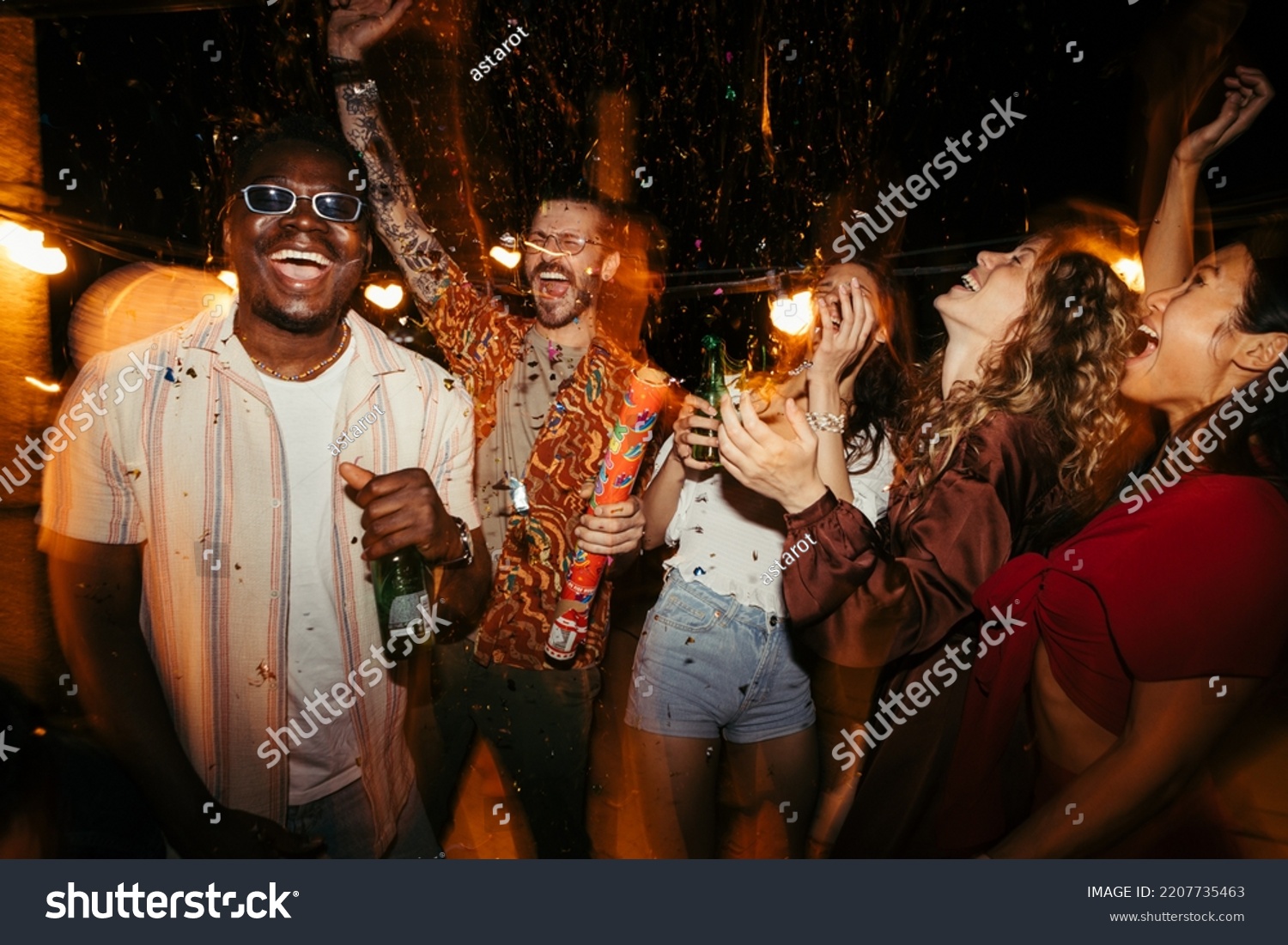 A cheerful group of people rejoices at the roof open-air nightclub and throws confetti. People are drinking, dancing and having a good time at the party. #2207735463