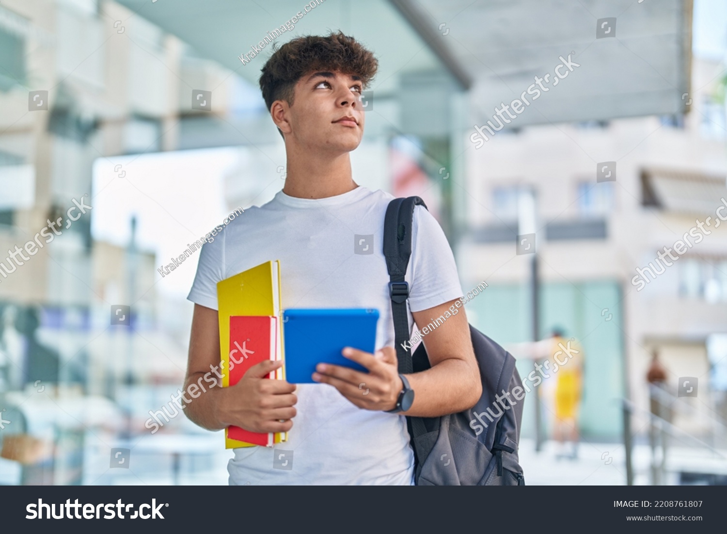 Young hispanic teenager student using touchpad holding books at university #2208761807