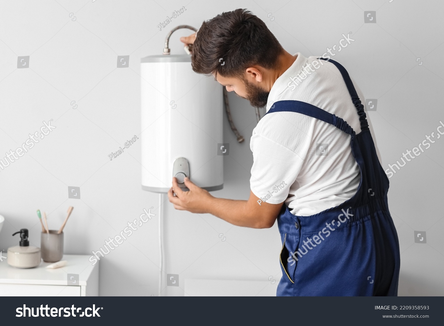 Male plumber adjusting boiler in bathroom #2209358593