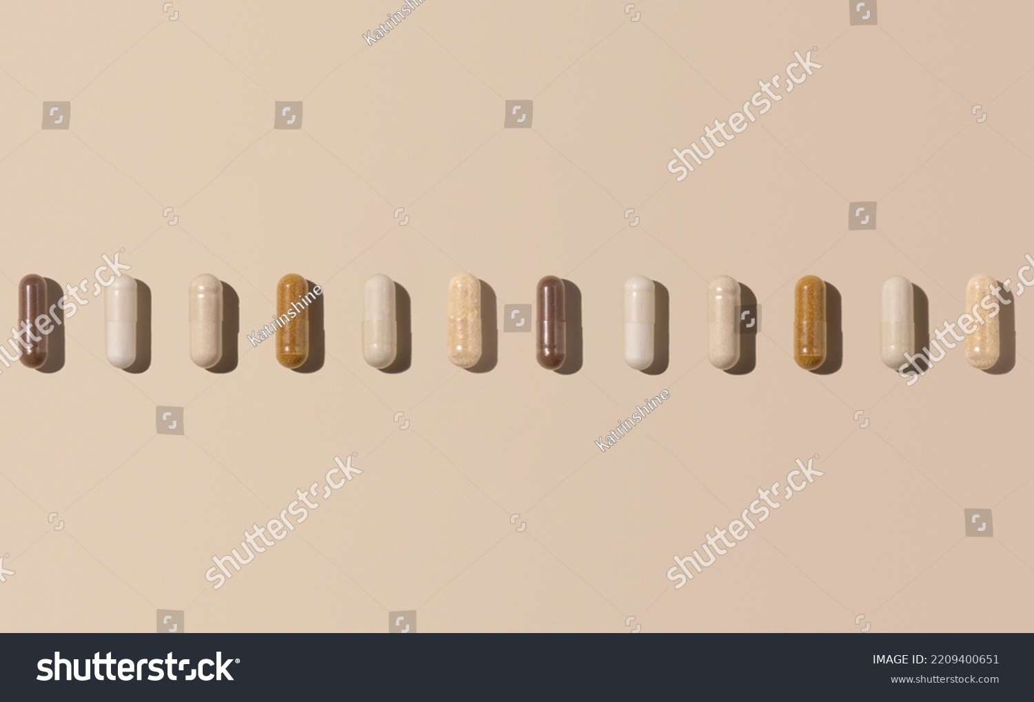 Mix of medical capsules in a line on light beige top view, hard shadows. Preventive medicine and healthcare, dietary supplements and vitamins.  Assorted pharmaceutical medicine capsules #2209400651