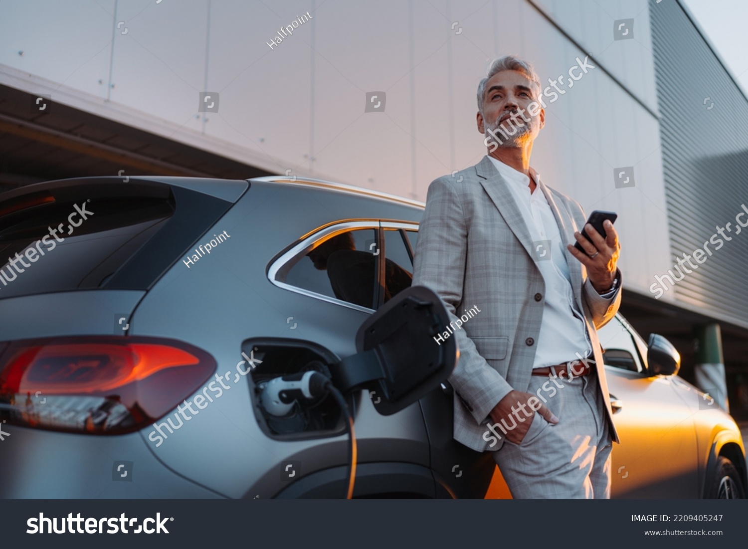 Businessman holding smartphone while charging car at electric vehicle charging station, closeup. #2209405247