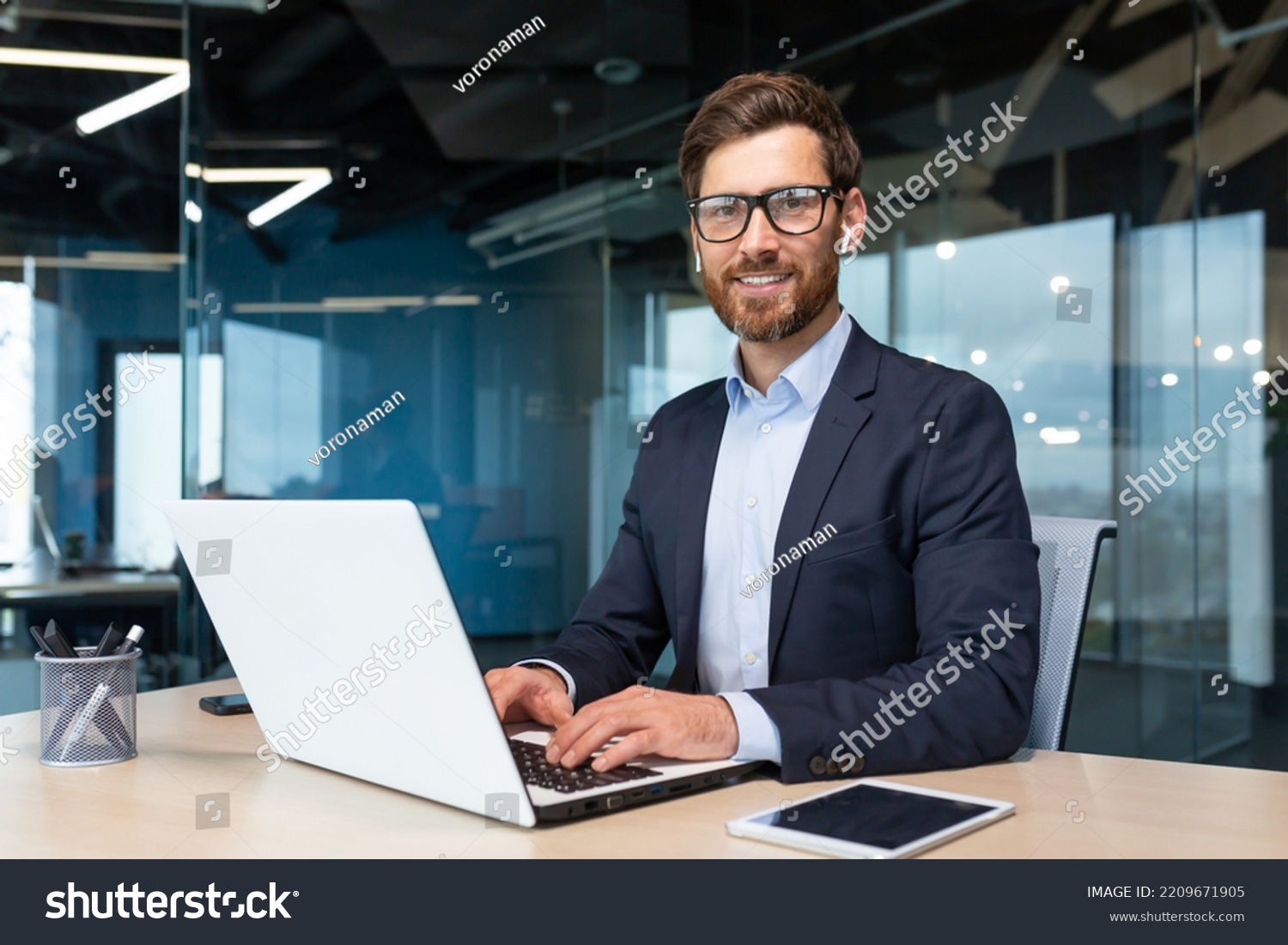 Portrait of mature boss inside office with laptop, successful and satisfied investor manager looking at camera and smiling man in glasses and business suit, investor with beard sitting on chair. #2209671905