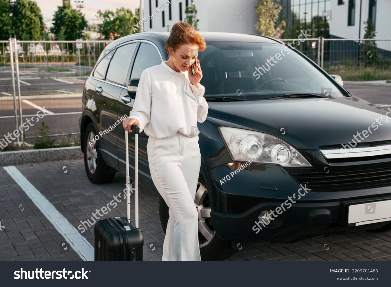 Stylish middle aged woman holding travel bag talking on mobile phone standing near new car. Business trip  concept	
 #2209701483