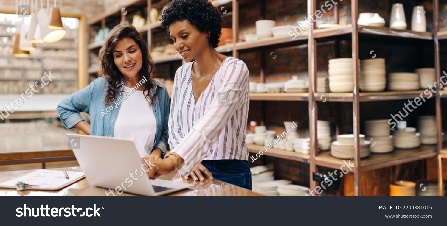 Young female ceramists using a laptop while working together. Two female entrepreneurs managing online orders in their store. Happy young businesswomen running a successful small business together. #2209881015