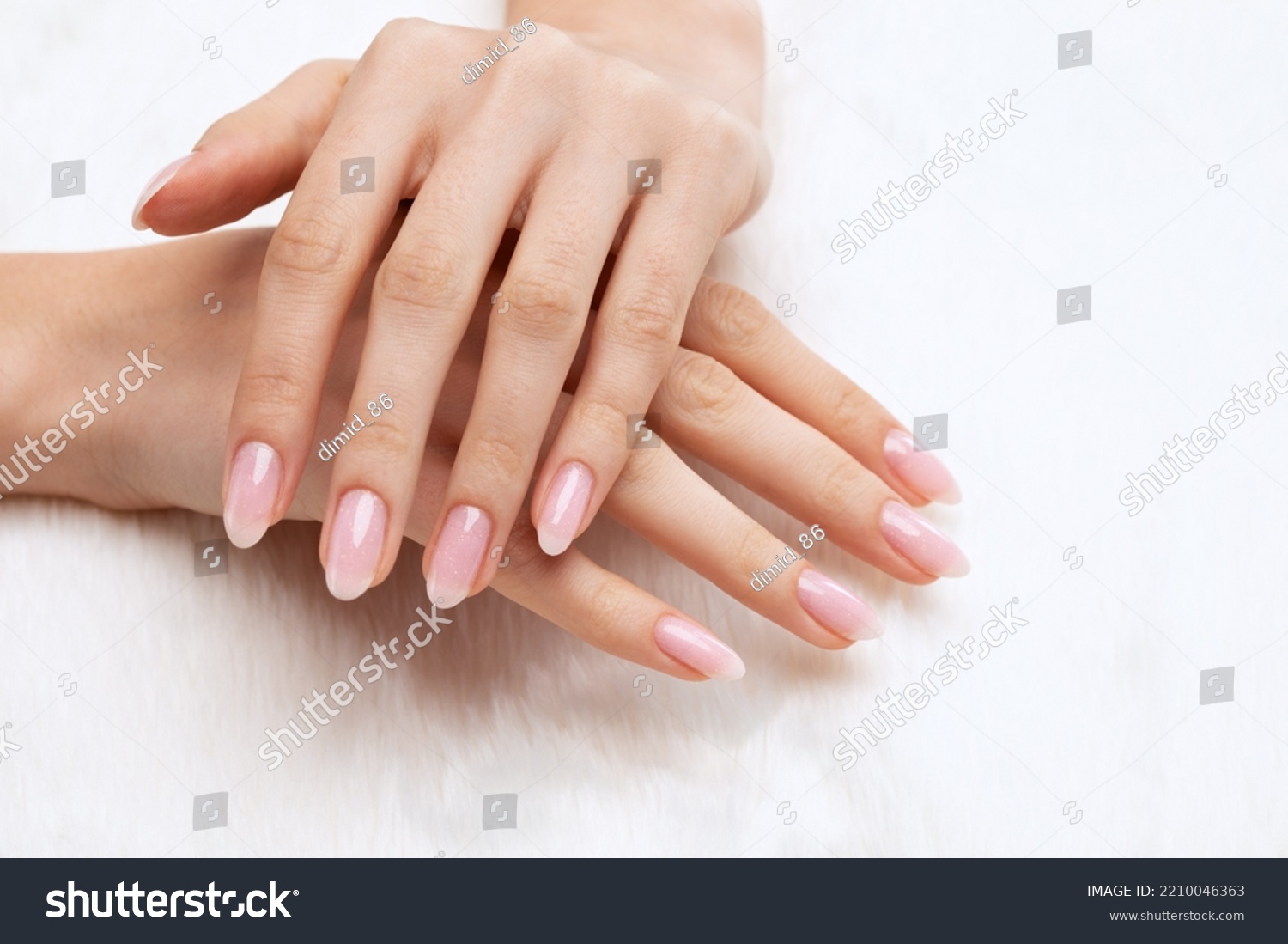 Girl's hands with a beautiful pale pink manicure. In the hands of white fur. the nail extension procedure in a beauty salon. Professional hand care. #2210046363