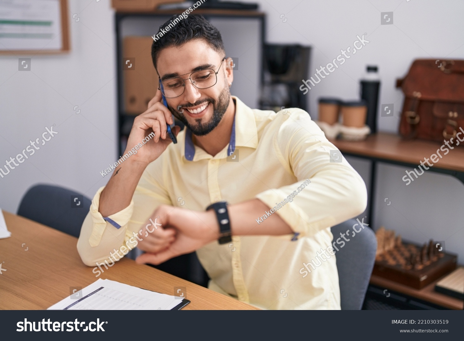 Young arab man business worker talking on smartphone looking watch at office #2210303519