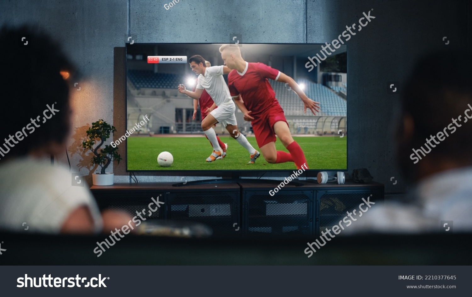 Black Couple Watches Professional Soccer Match on TV, Sitting on a Couch at Home in the Evening. Boyfriend and Girlfriend Football Fans Watch Sports. Back View Out of Focus Close Up Shot at Night. #2210377645